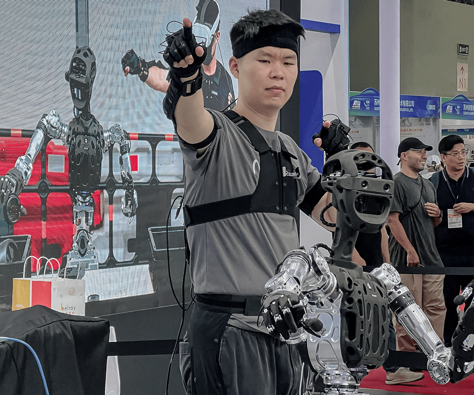 Operator using a motion-capture suit to teleoperate the Adam-U humanoid robot at the World Artificial Intelligence Conference 2025, demonstrating real-time embodied AI data collection with synchronized movement and tactile sensing.